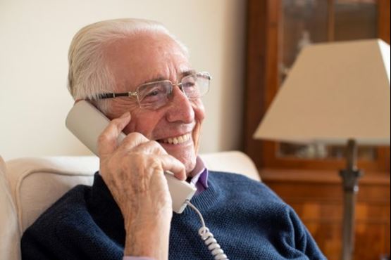 An older man sat at home on the phone - he is smiling