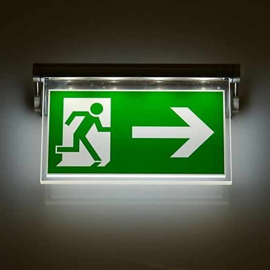 A green emergency exit sign is illumimated in a dark room