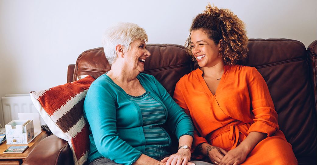 Resident and support officer smiling together on couch