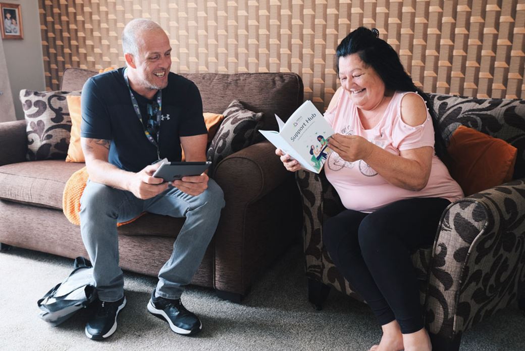 Prima Group employee with ipad sits in living room with resident