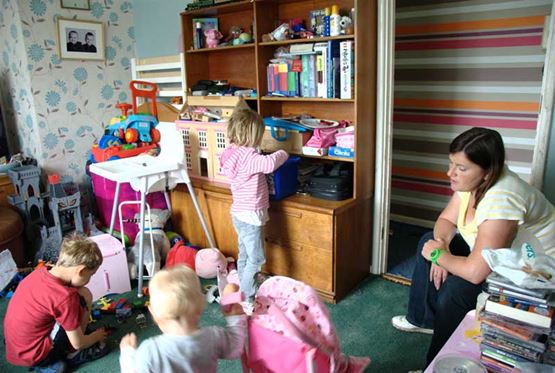 Mother in a room overcorwded with three children and not enough space for all the toys etc