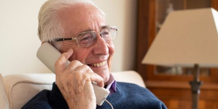 An older man sat at home on the phone - he is smiling