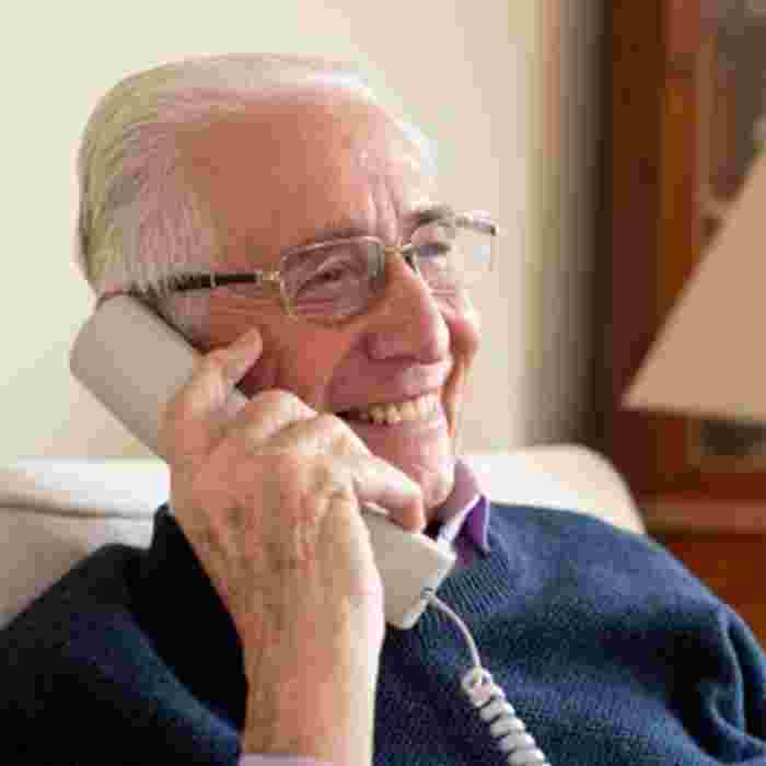 An older man sat at home on the phone - he is smiling