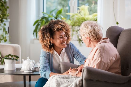 An older woman sits in a chair talking to a smiling younger woman