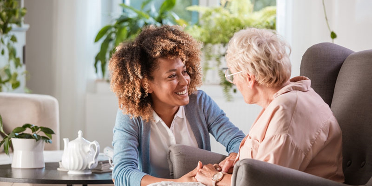An older woman sits in a chair talking to a smiling younger woman