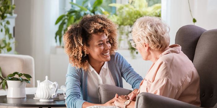 An older woman sits in a chair talking to a smiling younger woman