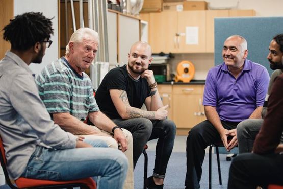 A small group of men dressed casually sit in a circle discussing something formally