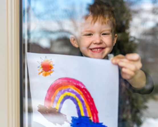 A child holds up a rainbow pictire to the window