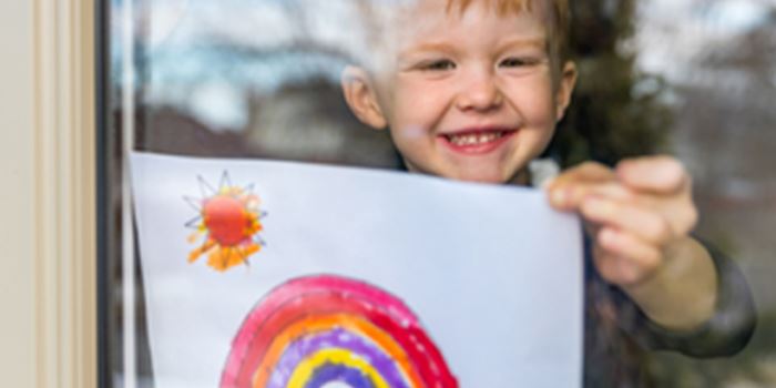 A child holds up a rainbow pictire to the window