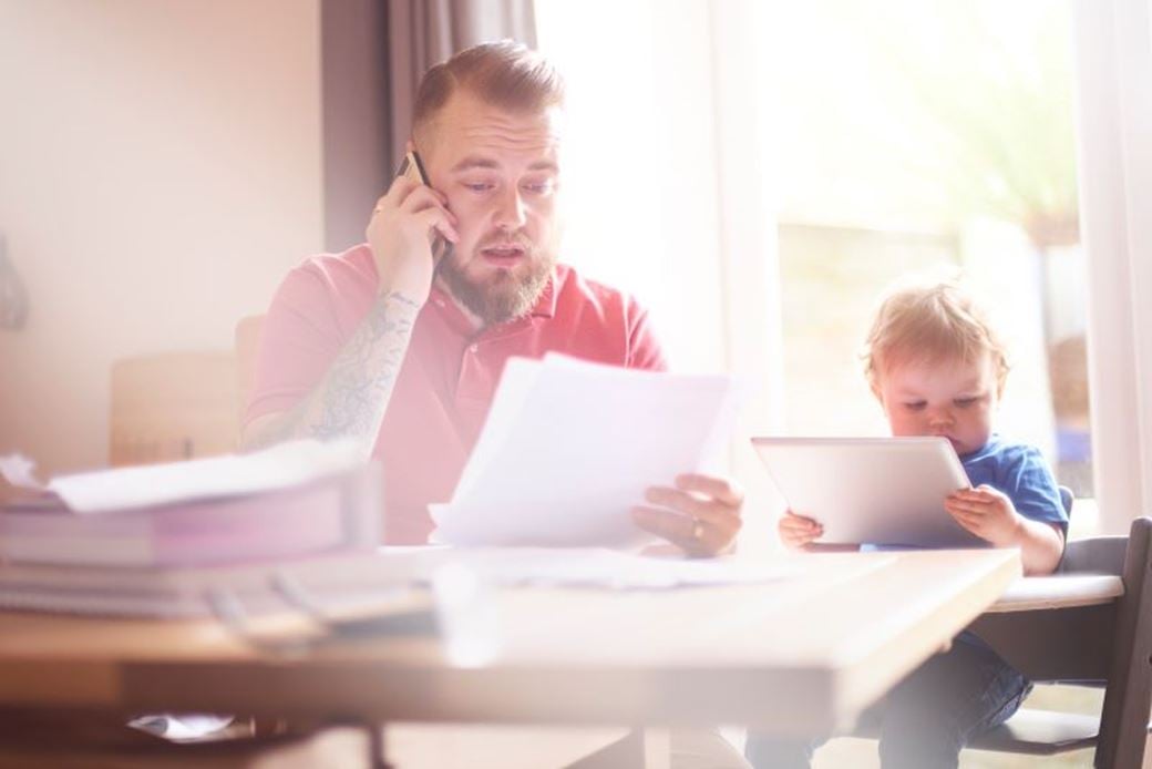 Man on phone look at bills with toddler sat beside him