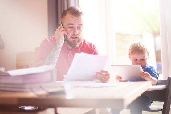 Man on phone look at bills with toddler sat beside him