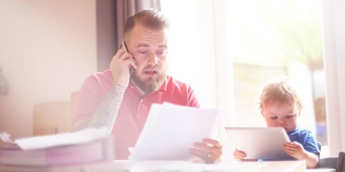 Man on phone look at bills with toddler sat beside him