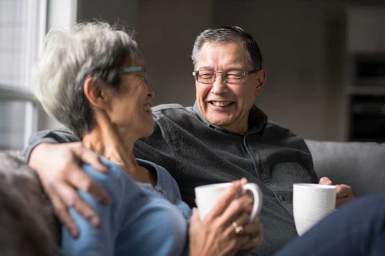 Couple in their 60s enjoy a cup of tea and a laugh on the sofa