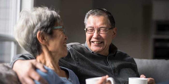 Couple in their 60s enjoy a cup of tea and a laugh on the sofa