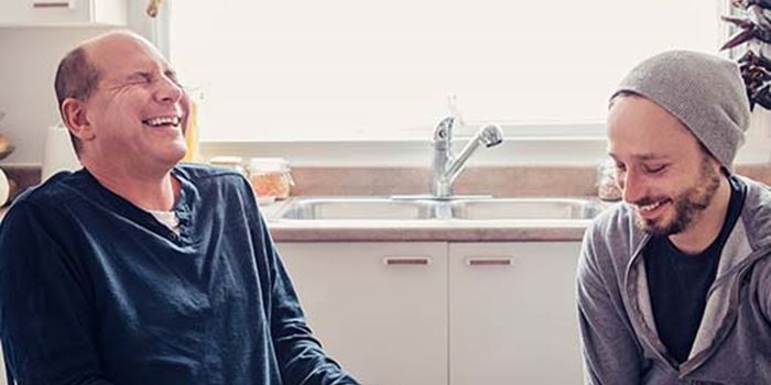 Photo of two men laughing around a kitchen table, one evidently a wheelchair user