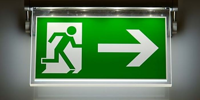 A green emergency exit sign is illumimated in a dark room