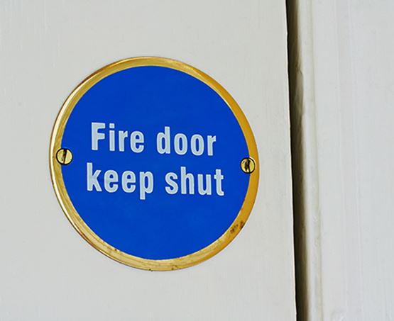 Round blue sign on a white door reads fire door keep shut