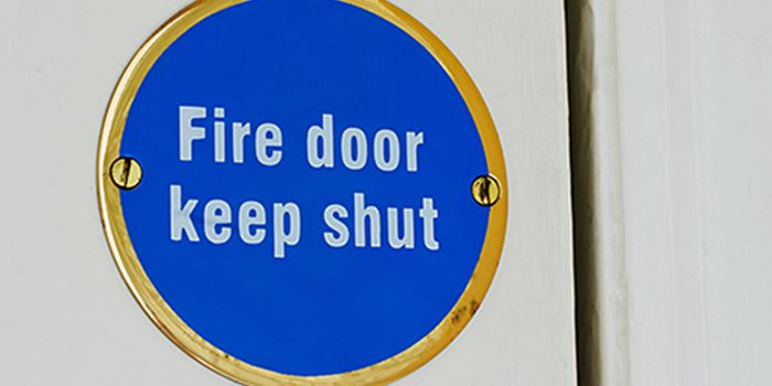 Round blue sign on a white door reads fire door keep shut