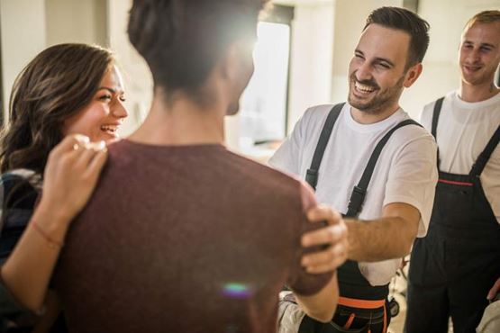 Smiling workmen in overalls are greeted by a couple