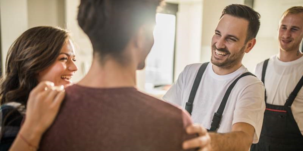 Smiling workmen in overalls are greeted by a couple
