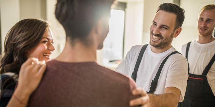 Smiling workmen in overalls are greeted by a couple