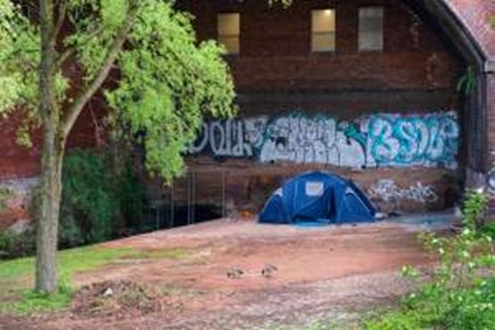 A tent pitched up next to a canal by front of a wall covered in graffiti