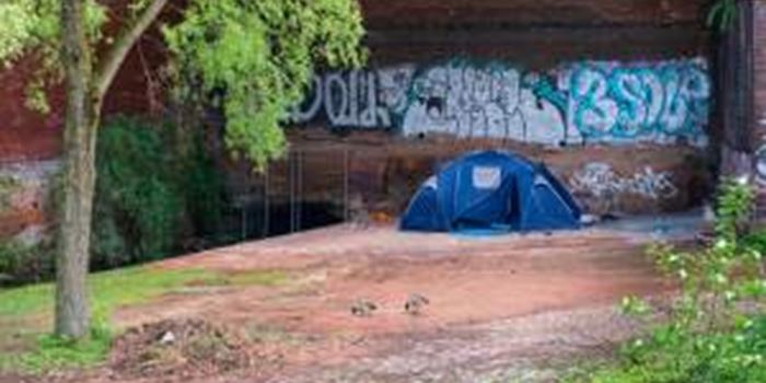 A tent pitched up next to a canal by front of a wall covered in graffiti