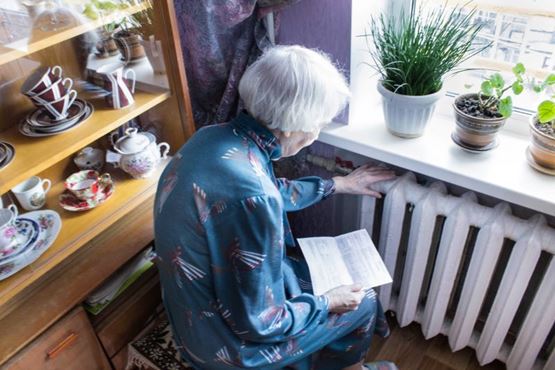 Older person close to a radiator looking at an energy bill