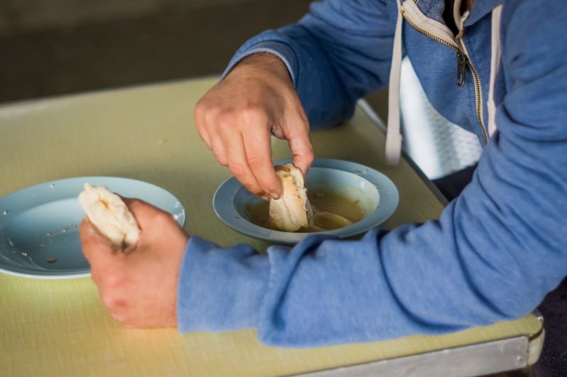 A man in a blue hoody eats soup with white bread