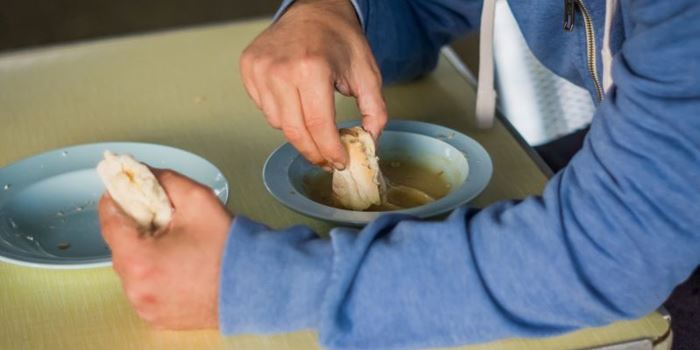 A man in a blue hoody eats soup with white bread