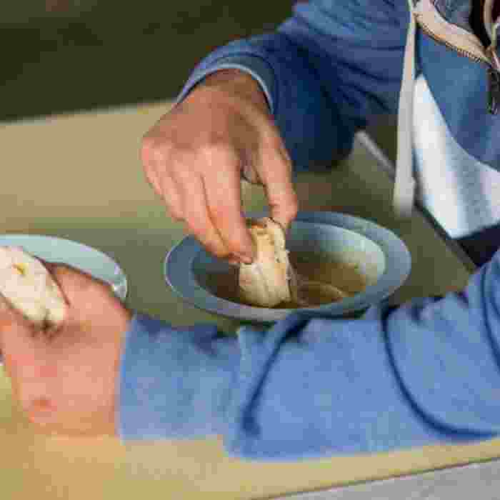 A man in a blue hoody eats soup with white bread