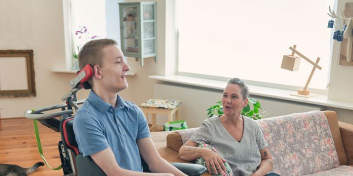 A young man in a wheel chair smiles while a woman sat next to him speaks and smiles