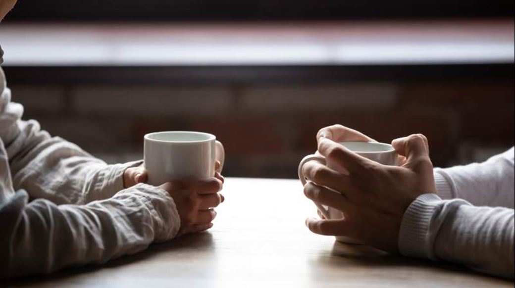 Two people facing each other holding hot drinks