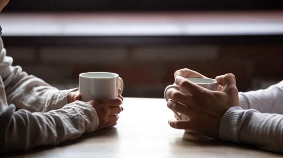 Two people facing each other holding hot drinks