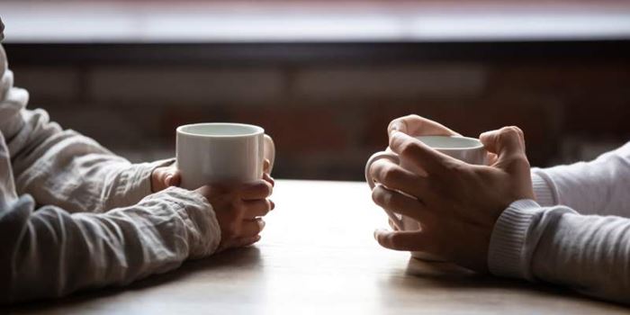 Two people facing each other holding hot drinks
