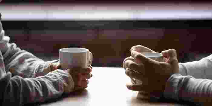 Two people facing each other holding hot drinks