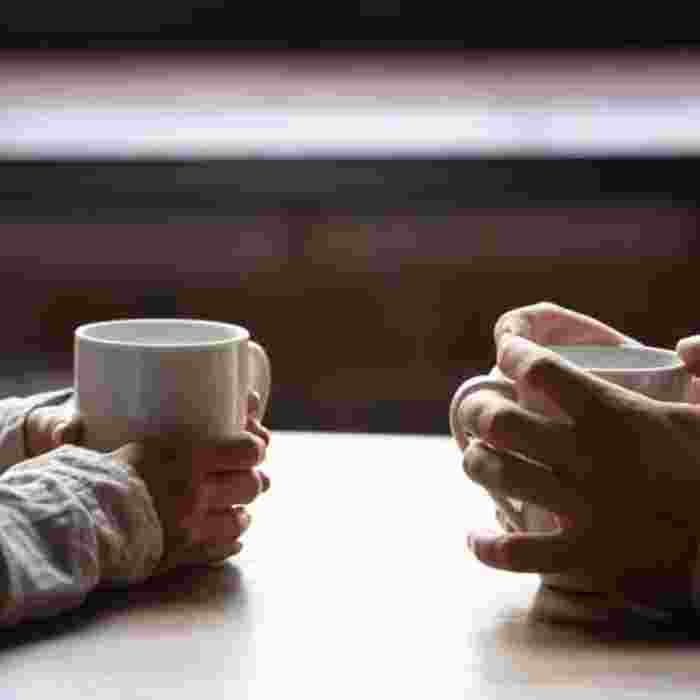 Two people facing each other holding hot drinks