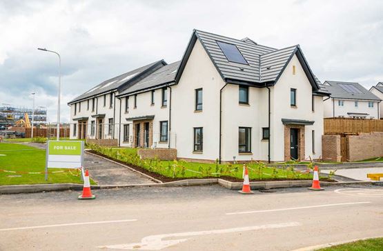 New houses with solar panels on roofs and a for sale sign outside