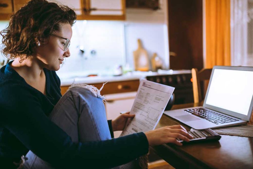 Woman in a kitchen with a utility bill, calculator and laptop