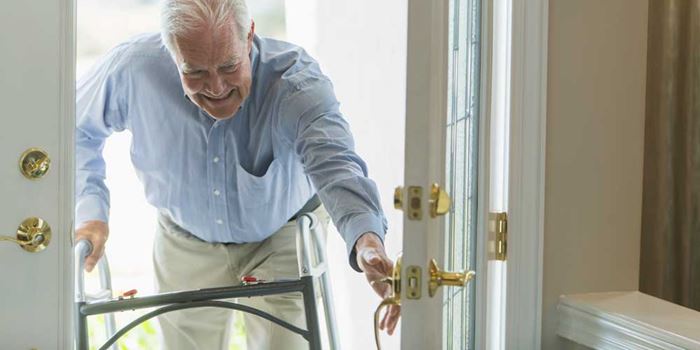 An older man with a walking frame smiles as he arrives home through the front door