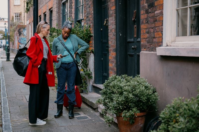 Two women looking at tablet outside houses